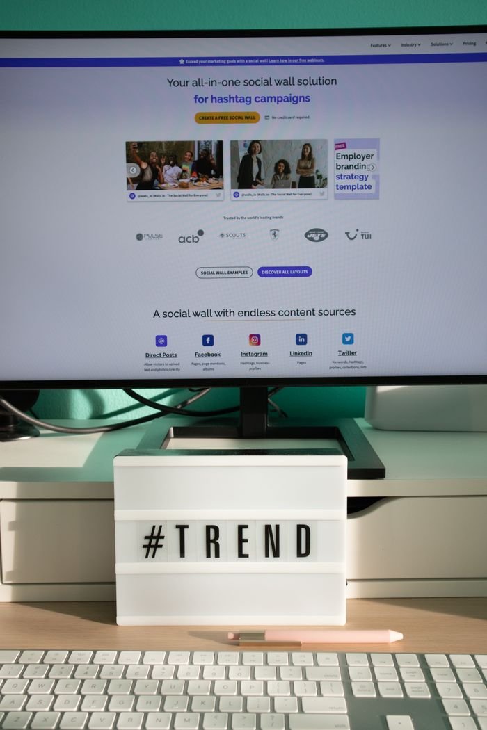 A clean and modern desk setup with a lightbox displaying '#TREND' and a computer monitor showing a social wall solution.