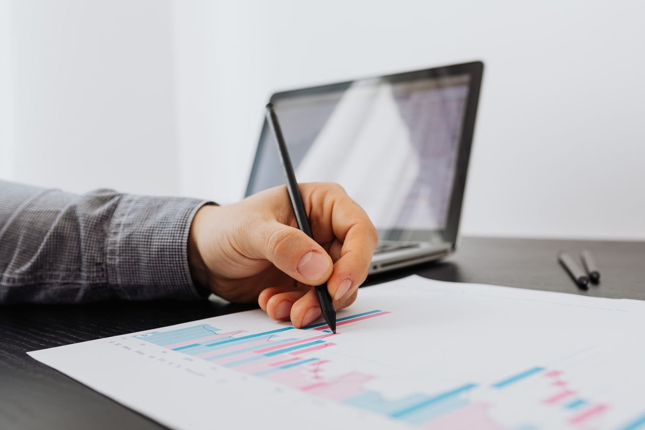 our-services-1 Person taking notes on a business chart with a laptop in the background.