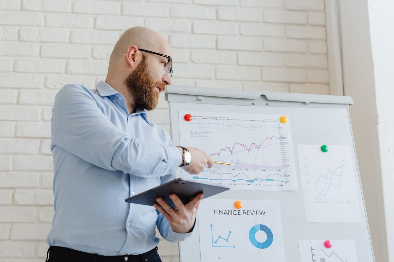 our-services-1 Man giving a business presentation with financial graphs on a whiteboard using a tablet for explanation.